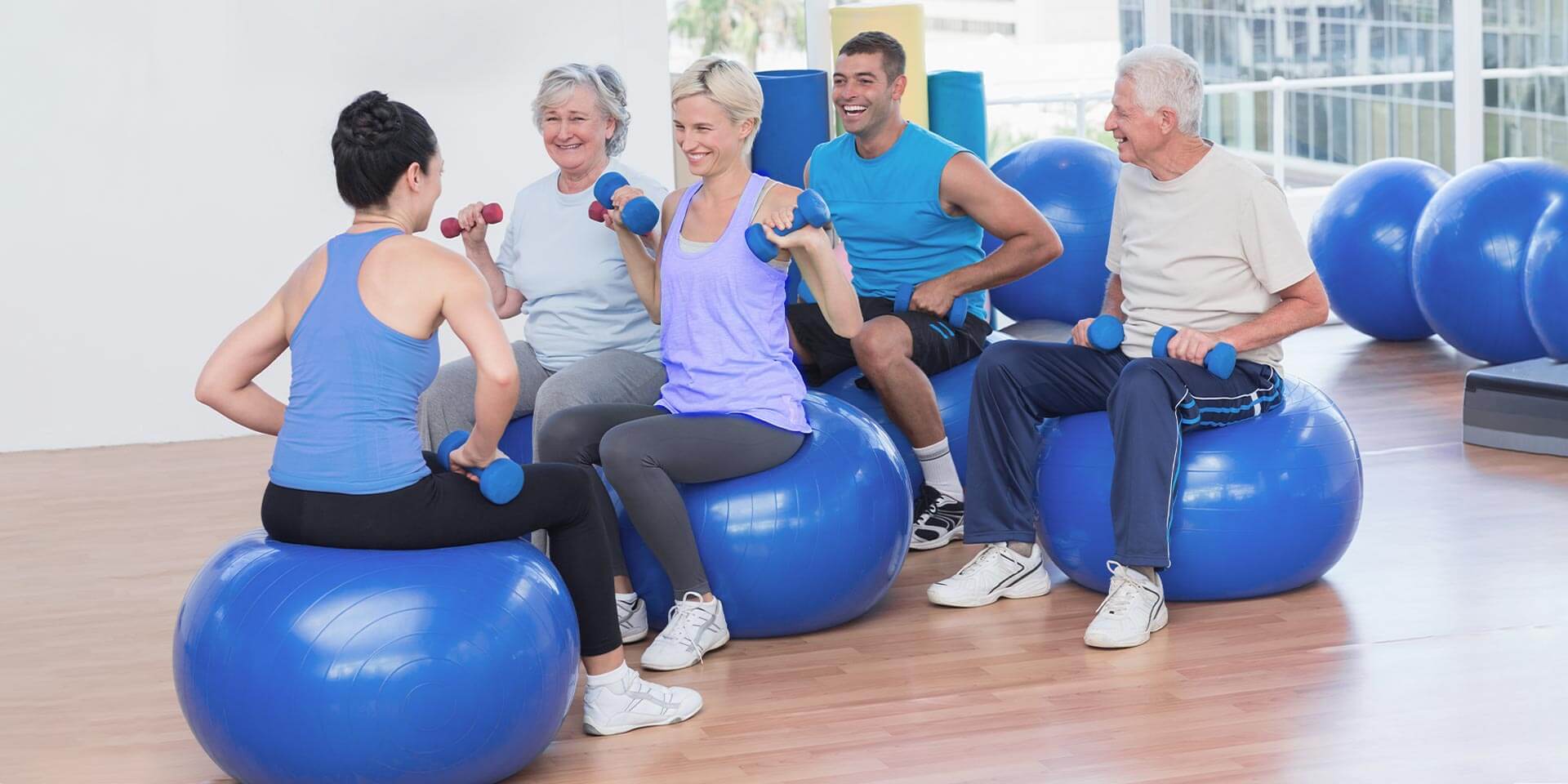 Physiotherapeutin mit Kursgruppe beim Training mit Gymnastikball und Hanteln